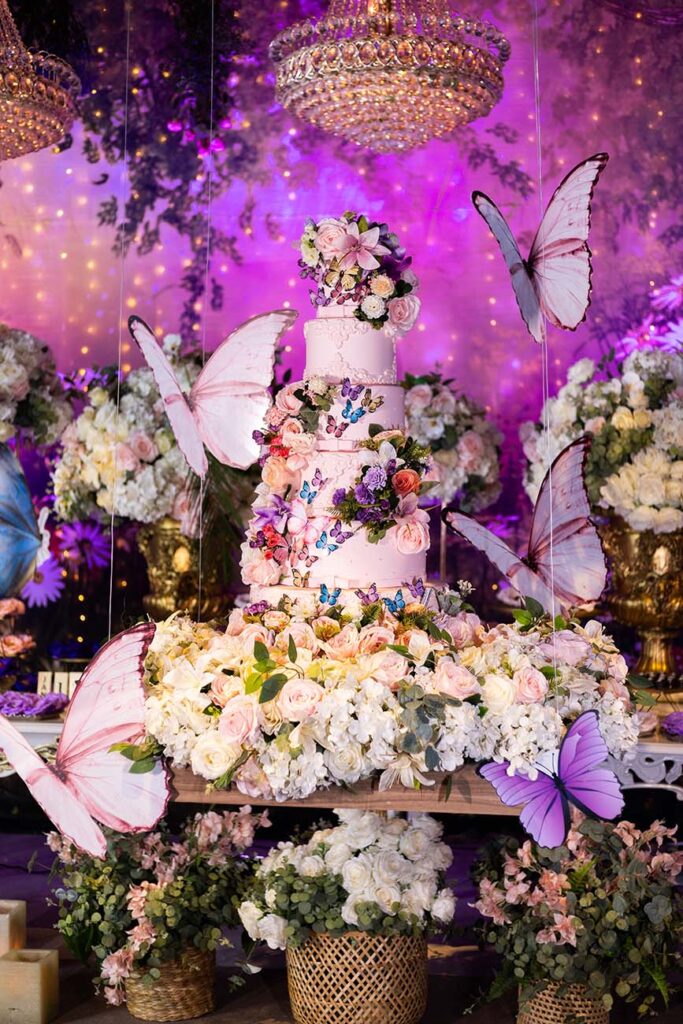 Mesa do bolo decorada com borboletas, flores e iluminação em roxo