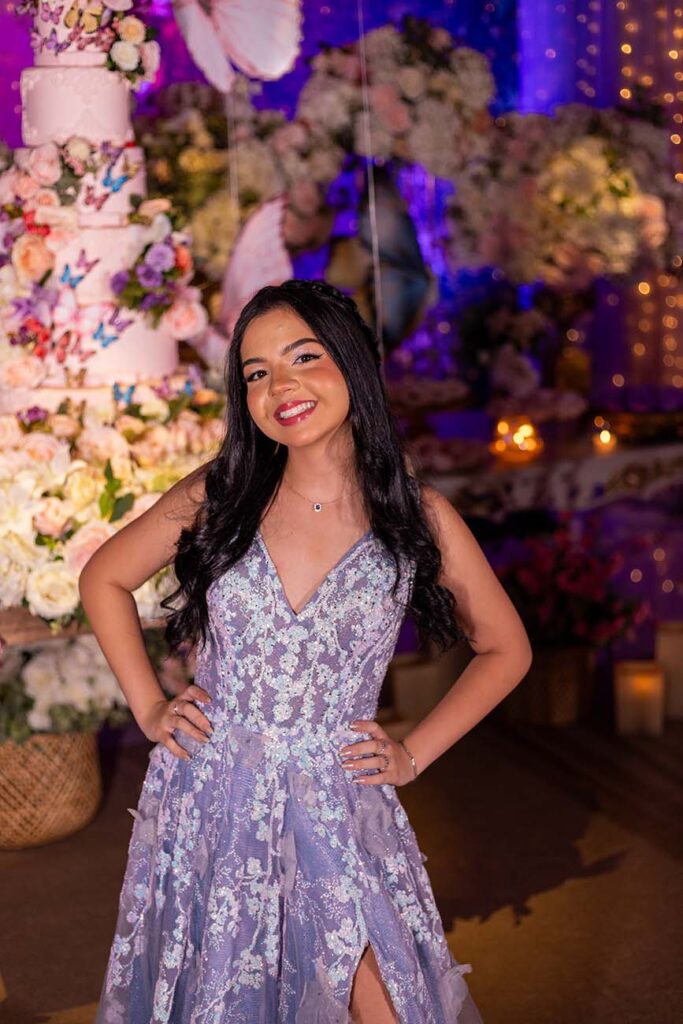 Debutante no segundo look prateado diante do cenário de flores