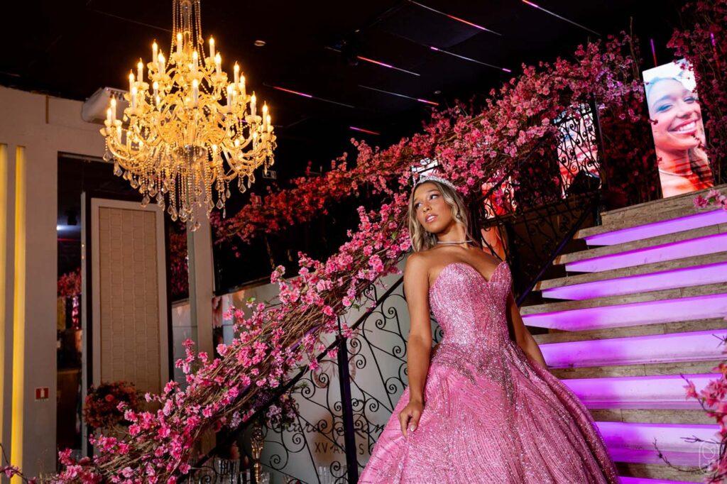 Debutante em vestido rosa na escadaria decorada com flores