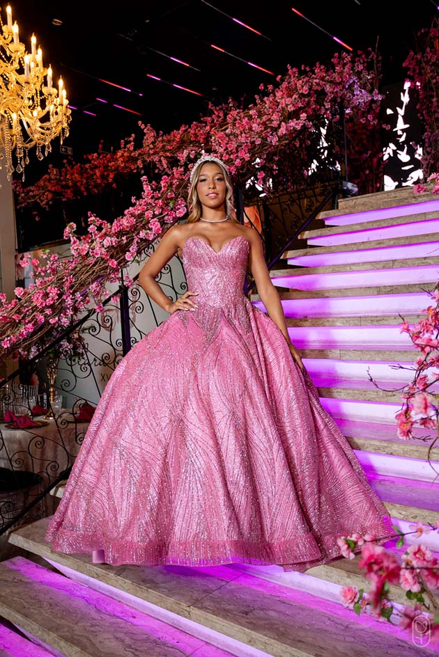 Debutante em vestido rosa ao lado da escadaria iluminada