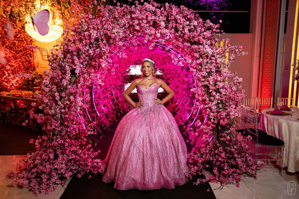 Debutante em vestido rosa sob o arco florido em tons de pink