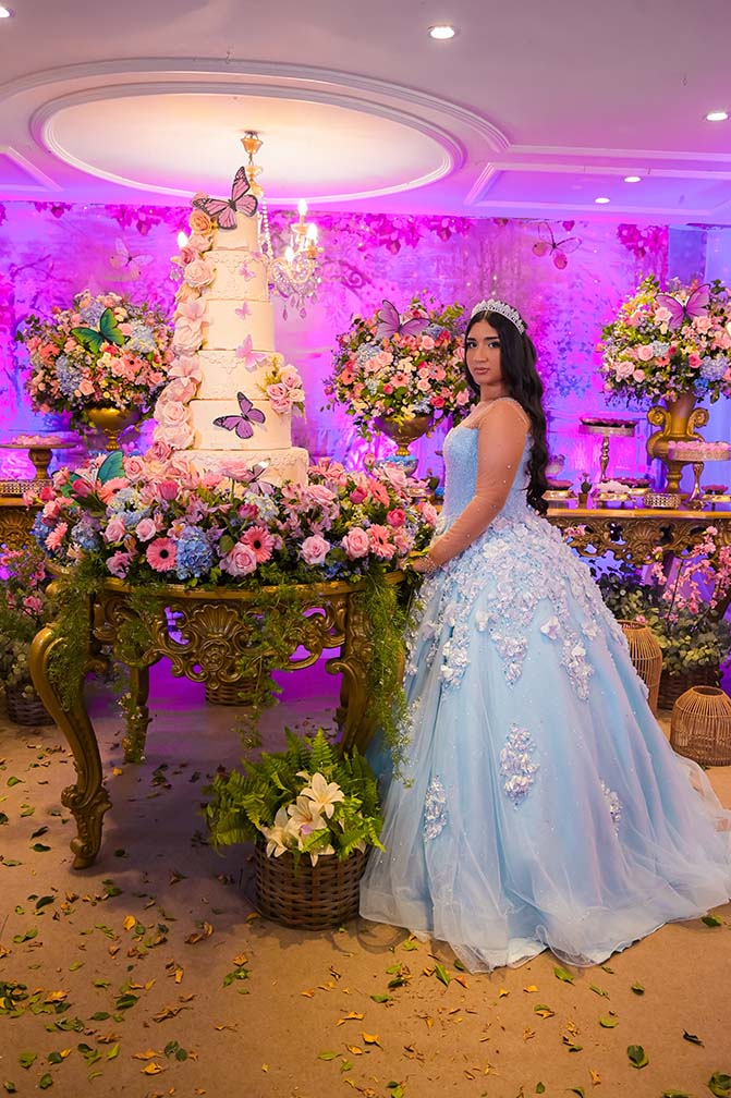 Debutante em vestido azul ao lado da mesa do bolo