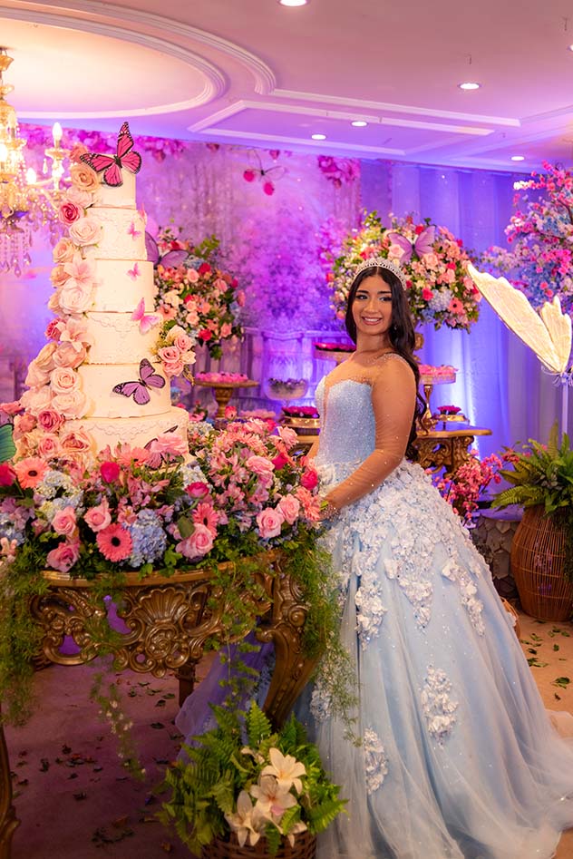 Maria Eduarda em vestido azul diante da mesa do bolo com borboletas