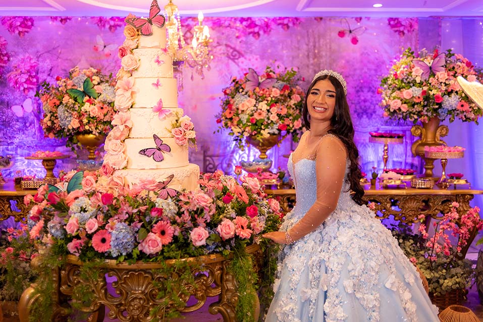 Debutante em vestido azul ao lado do bolo decorado com borboletas