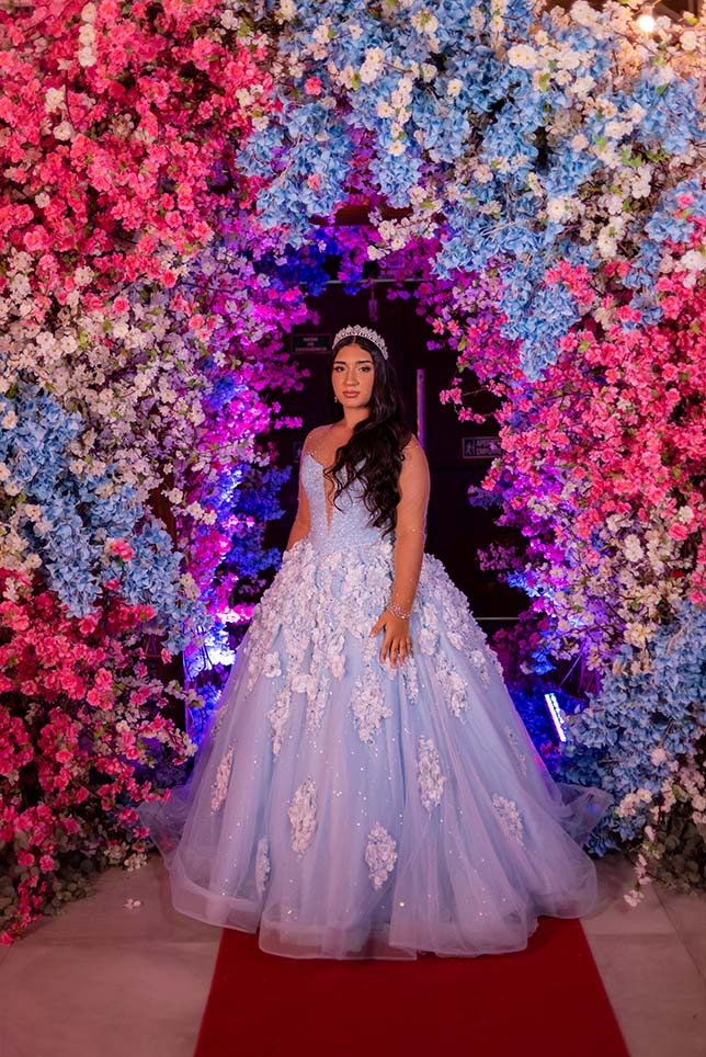 Debutante em vestido azul emoldurada pelo arco florido