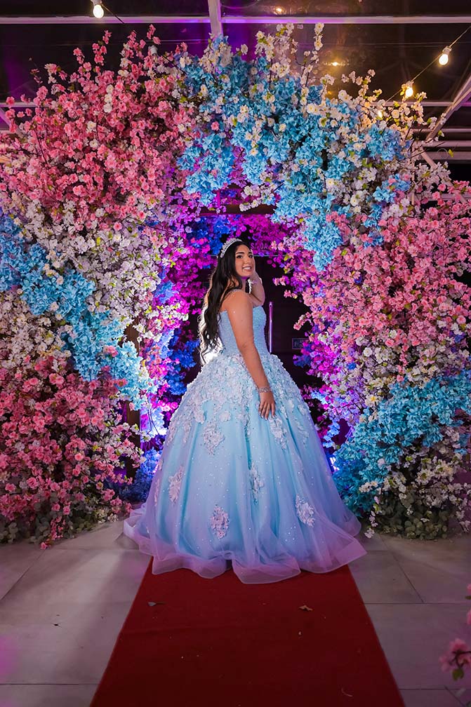 Debutante em vestido azul no tapete vermelho sob o arco de flores