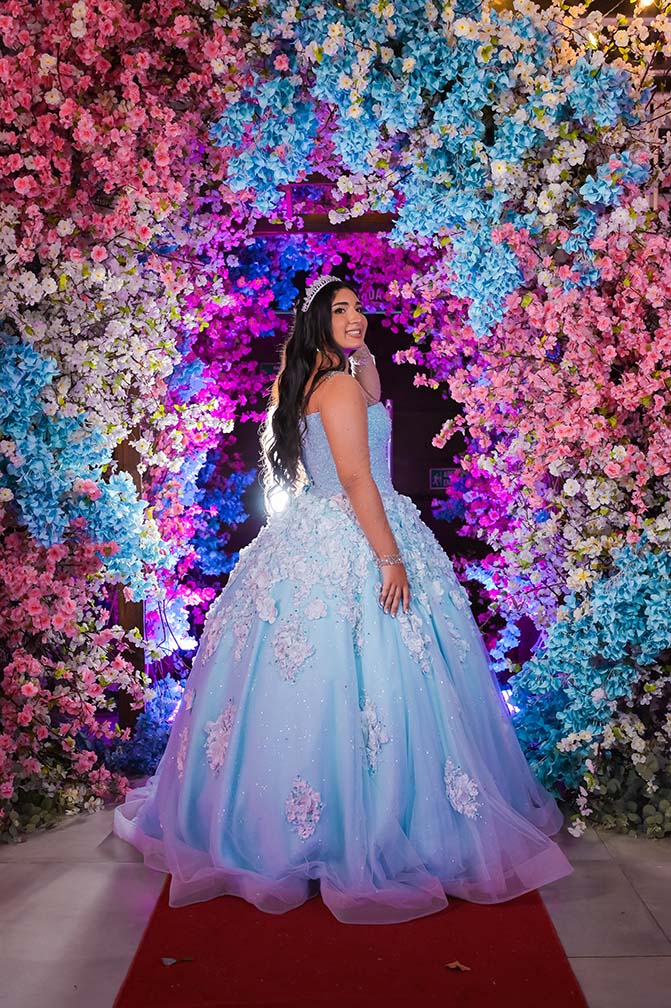 Debutante em vestido azul entre as flores do arco decorado