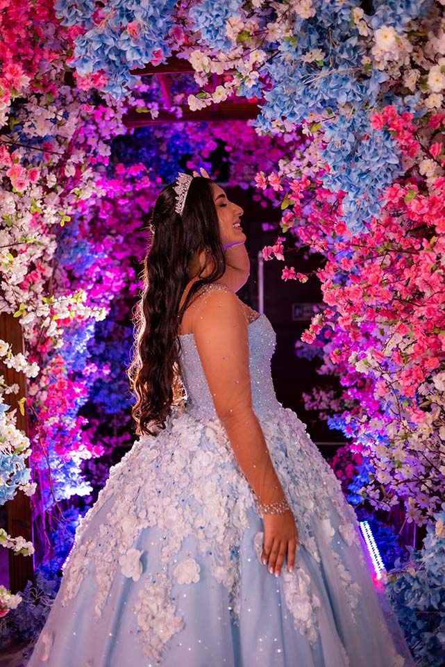 Debutante em vestido azul diante do arco de flores iluminado