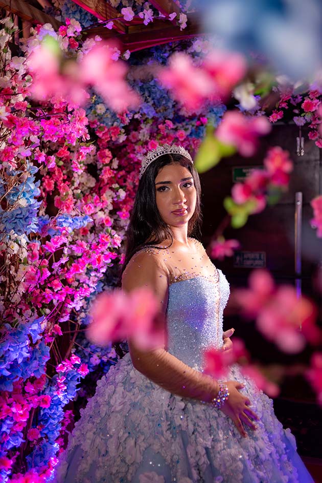 Debutante em vestido azul entre flores em tons de rosa