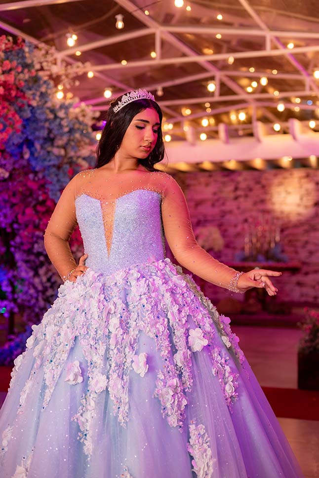 Debutante em vestido azul sob as luzes suspensas do arco florido