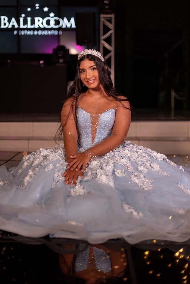 Debutante sentada com o vestido azul diante do letreiro da casa de festas