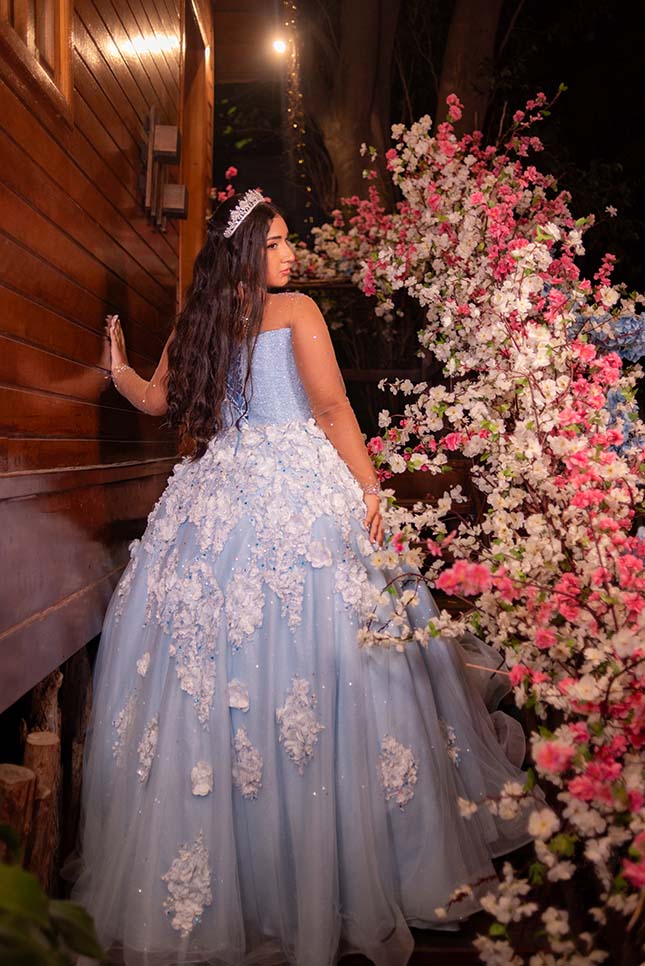 Debutante em vestido azul ao lado da parede de flores