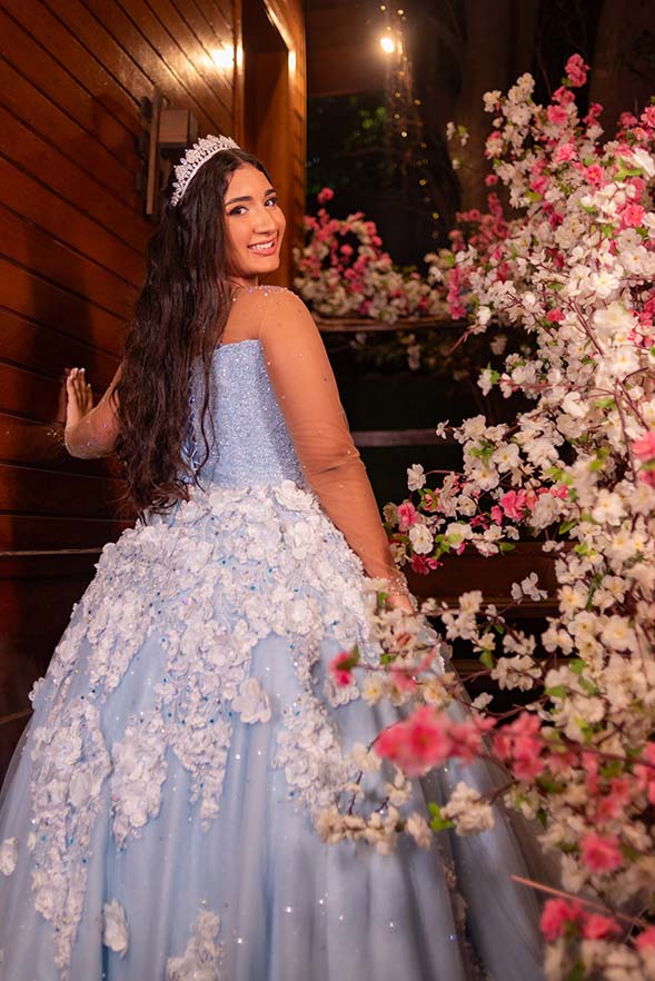 Debutante em vestido azul diante da parede florida do cenário