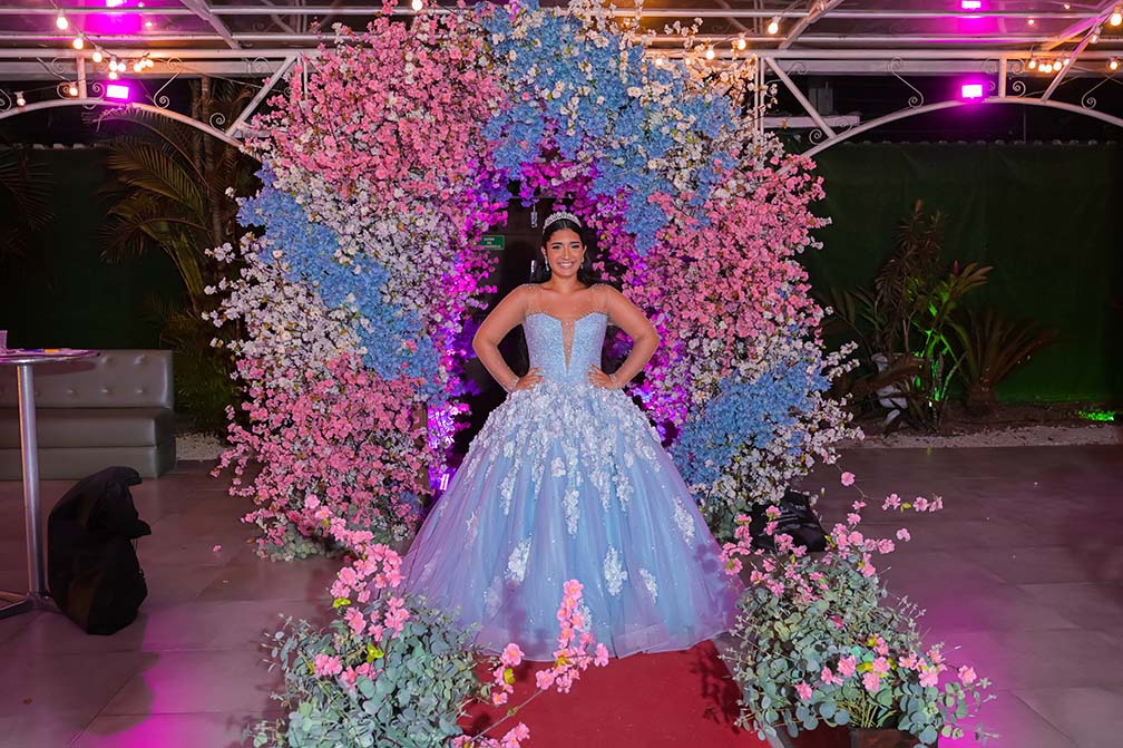 Debutante em vestido azul sob o arco de flores da área externa