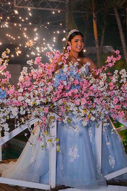Debutante em vestido azul entre as flores sob a chuva de prata