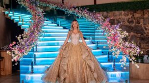 Debutante em vestido dourado na escadaria iluminada em azul com arco floral na festa de 15 anos tema Aladdin