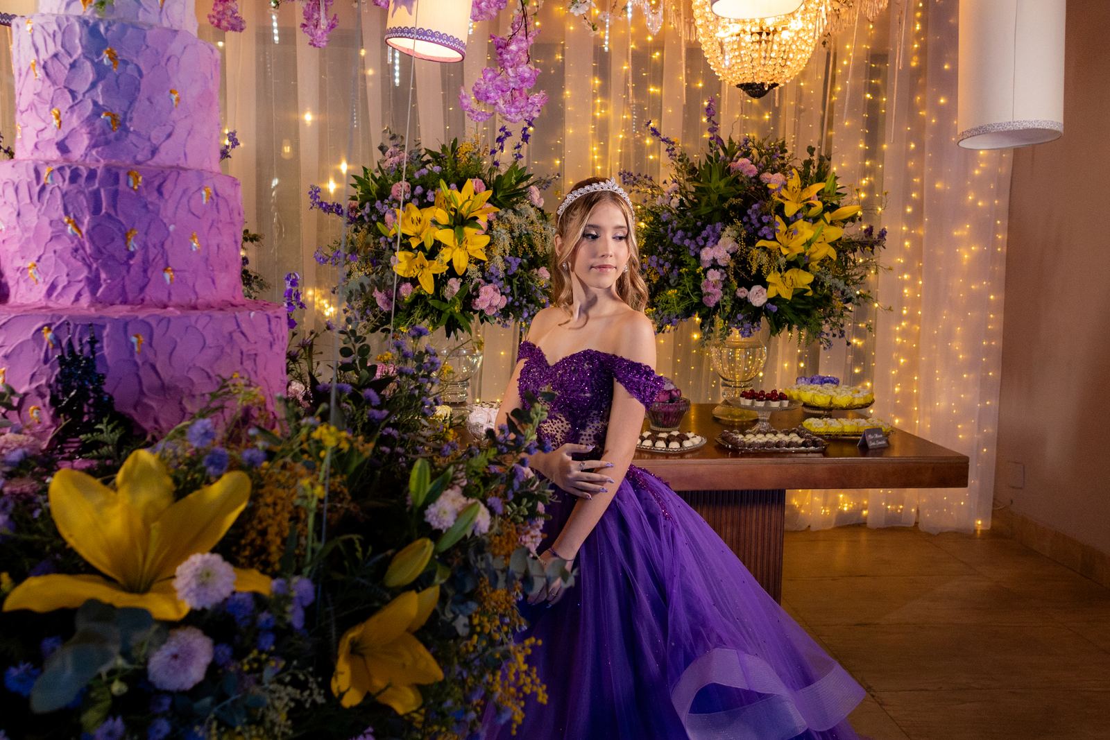 Debutante em vestido roxo ao lado do bolo de 15 anos em tons de lilas
