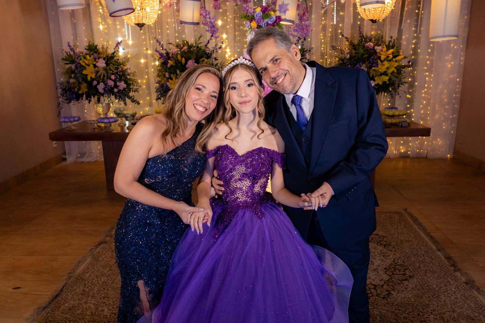 Debutante entre os pais diante da mesa do bolo na festa de 15 anos